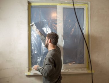 Sakallı bir adam pencere yamaçlarında spatula ve macun var.