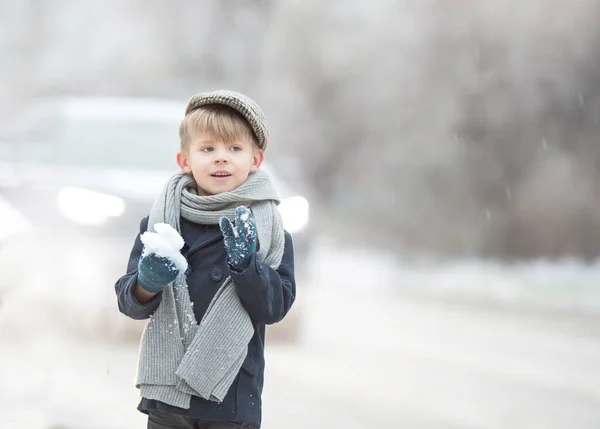 a boy in vintage clothes is standing by the road, he is cold, he is shivering, winter and sno