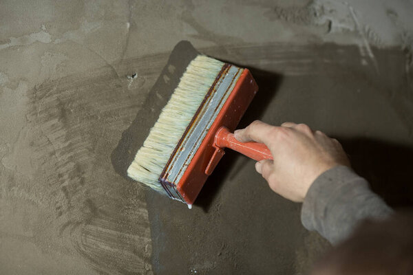 Рука мужчины крупным планом грунтует бетонную стену старой кистью перед стеной