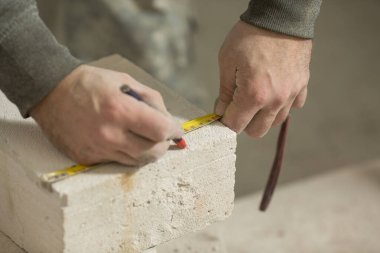 Erkek bir inşaat işçisi havalandırma beton duvarını bir bant mezurasıyla ölçer.
