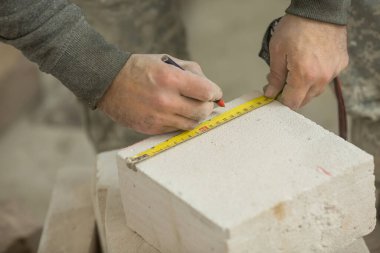 Erkek bir inşaat işçisi havalandırma beton duvarını bir bant mezurasıyla ölçer.