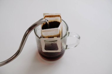 Cam bardakta demlenmiş su torbası kahvesi. Kaz boynu çaydanlığından su dökülüyor. Anında taze kahve yapma yöntemi. Beyaz tablo