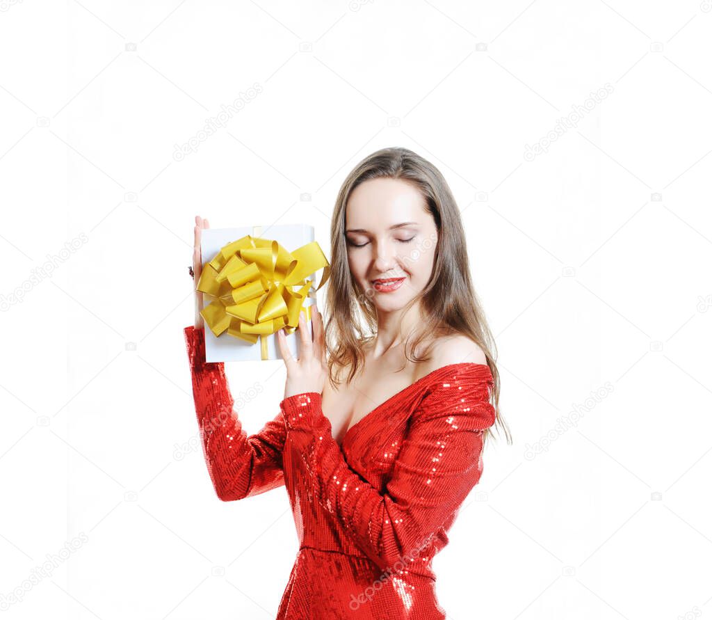 Beautiful girl in red shiny dress dreamily holding a wrapped gift. Holiday party concept, isolated on white, copy space