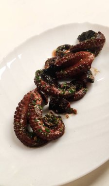 Beyaz bir tabakta servis edilen doğranmış bitkilerle pişirilmiş ahtapot.