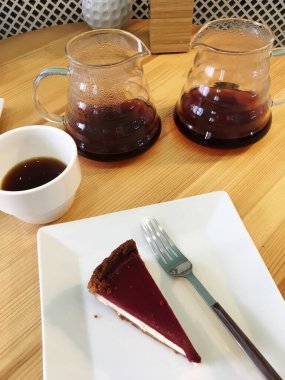 Kafedeki ahşap masada servis edilen iki bardakta taze siyah filtre kahve. Beyaz tabakta peynirli kek. Özel kahve.