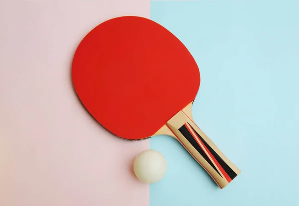 Red table tennis racket and ping pong ball on pink blue. Sport concept