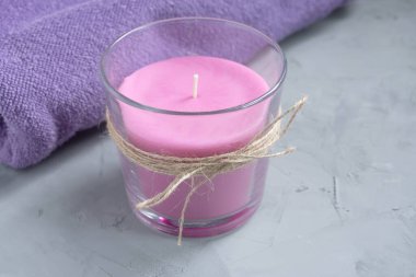 Bir pembe mum ve gri arka planda bir leylak havlu. Aroma ve spa terapisi kavramı