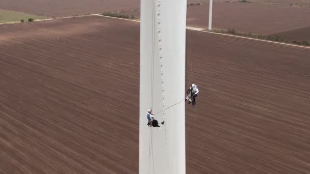 Workers couple repairs wind driven turbine near plowed field — Stock Video