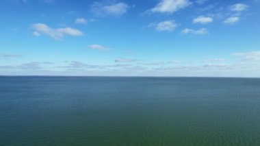 Parlak mavi gökyüzü, sınırsız berrak okyanus suyunun üzerindeki bulutlar.