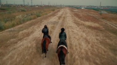 Kadın arkadaşlar dört nala at sırtında zemin yolunda oturuyor.