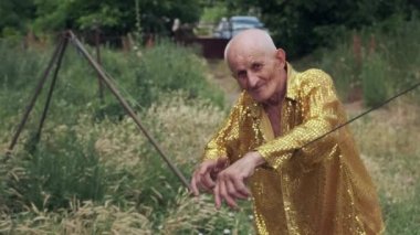 Very old man in bright golden festival shirt with sequins looks straight with satisfied face expression. Pensioner smiles enjoying life closeup