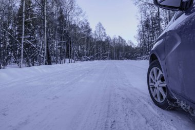 Car tires on a winter snow - covered forest road . Winter landscape with a blue car in the forest.