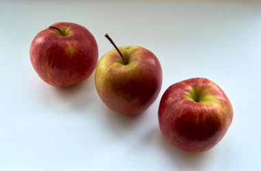 Beyaz bir zemin üzerinde doğal ışık altında olgun kırmızı elmalar.