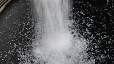 Siyah bir tabağa beyaz şeker dökülüyor, tatlı, sağlıksız yiyeceğe bağımlılık kavramı, obezite. Tatlı malzemesi