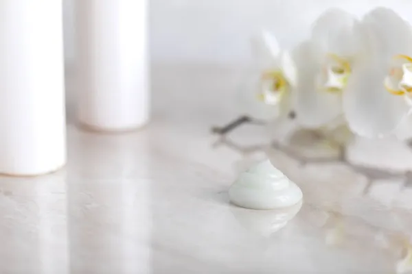 Licht Schönheit Hintergrund mit weißen Orchideenblüten, Creme Textur und weißen Flaschen, Konzept der Naturkosmetik für Körper, Gesicht und Haare — Stockfoto