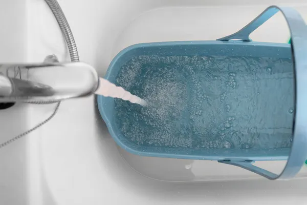 El agua limpia del grifo en el baño se vierte en un cubo azul para limpiar y fregar de cerca, vista superior —  Fotos de Stock
