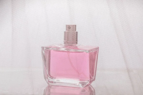 Glass bottle of gentle pink perfume without a lid on a light background behind a mesh transparent texture of fabric in blur, the concept of expensive perfumery and cosmetics, a gift for women — Stock Photo, Image