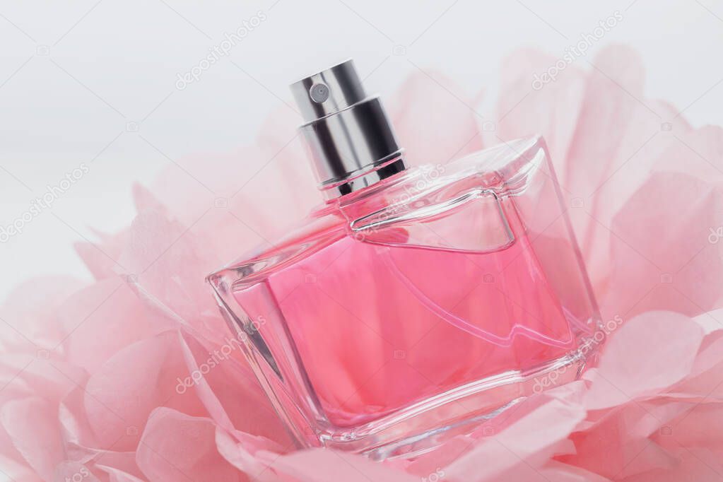 glass bottle of delicate pink perfume on the background of thin paper flower petals, beauty concept of perfumery and womens cosmetics, a gift for a holiday, March 8 or womens day