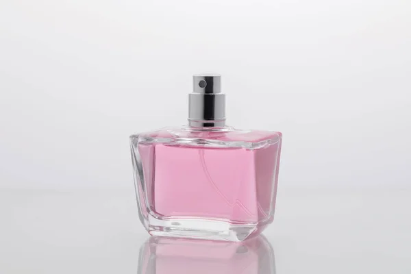 Glass bottle of delicate pink perfume on a light background with reflection on the table, minimalistic beauty concept of perfumery and womens cosmetics, a gift for a holiday, March 8 or womens day — Stock Photo, Image