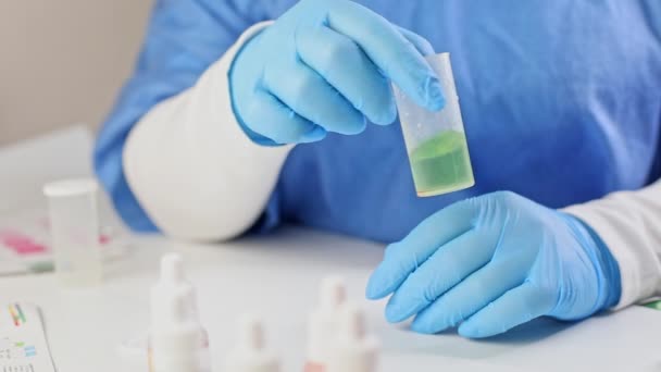 Βοηθός εργαστηρίου με μπλε ιατρική στολή και γάντια διεξάγει δοκιμές νερού, αναμιγνύει το πράσινο αντιδραστήριο με νερό ενυδρείου σε δοχείο για χημικά πειράματα, ελέγχει την ποιότητα του υγρού — Αρχείο Βίντεο