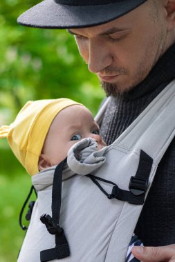 Baba, çocuğunu bebek askısıyla taşırken.