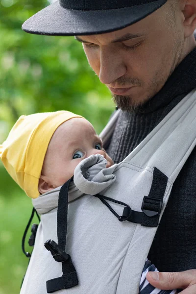 Baba, çocuğunu bebek askısıyla taşırken.