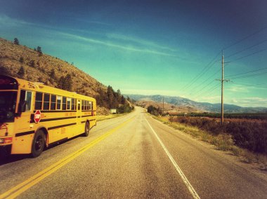 View of a passing school bus from a passengers perspective looking through the windshield overlooking the Canadian landscape of the Okanagan Valley in Osoyoos, British Columbia, Canada. This perspective is the concept of van life, travel, and wanderl