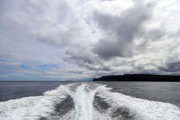 An outboard motor wake from a cruising powerboat on the sea in a seascape with the horizon over water on a cloudy day at Langara Island located in Haida Gwaii, British Columbia, Canada.