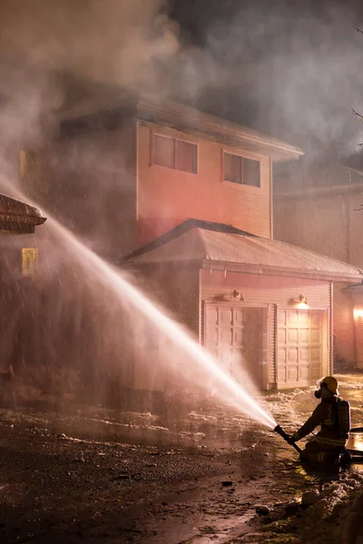 Squamish, British Columbia, Canada - December 12, 2016: Fireman extinguishing a house fire at night in a townhouse complex in Squamish, British Columbia, Canada.