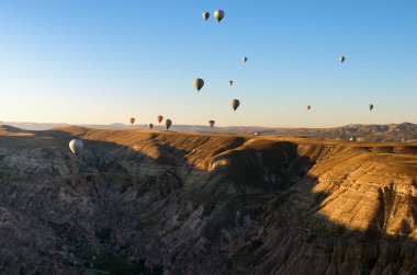 Goreme, Türkiye-9 Ekim 2021: Kapadokya 'da sıcak hava balonları festivali. Canlı gökyüzüne karşı bir sürü renkli balon. Arka planda olağandışı kaya oluşumlu sonbahar manzarası.