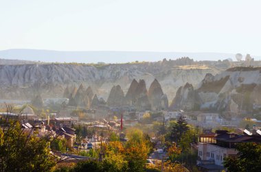 Antik Goreme 'in sonbahar hava manzarası. Cappadocia 'nın ünlü mağara kasabası. Arka planda hafif sis ve dağlar olan pitoresk bir şehir. Güneşli sonbahar sabah manzarası.