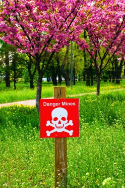 Tehlike mayınları işareti. Beyaz harfli kırmızı tabak, kafatası ve çapraz kemikler. Arka planda bulanık sakura ağaçları var. 2022 ilkbaharında Ukrayna, Kyiv 'de. İşgalcilerden korunma şehri kavramı.