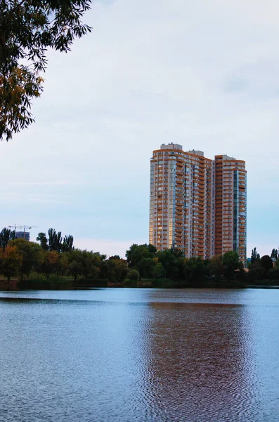 Modern skyscraper reflected in the tranquil water of Telbin Lake in Kyiv. Tree leaves boarder. Nature composition. Blue sky background.