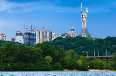 Famous Motherland Monument (Rodina mother) on stormy sky and gloomy clouds background. Unfinished multi-story apartment buildings in the background.