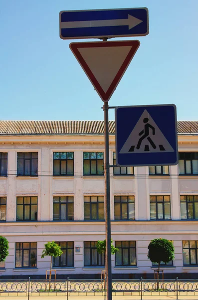 Traffic signs on the street. A one-way street sign. Give way road sign. The crosswalk sign. Blurred cityscape in the background.