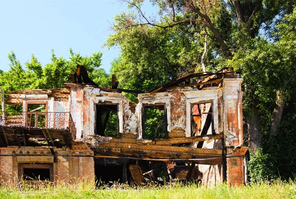 A house destroyed by fire. Ruins of old wooden house after fire. Abandoned two-storey house without roof and flor of second storey. Tree leaves boarder. Summer sunny morning view.