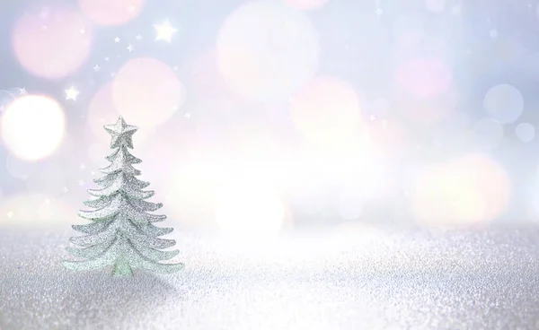 Winter christmas scenic background. Silvery small Christmas tree on a blurred snowy defocused background in blue and pink tones with copy space.