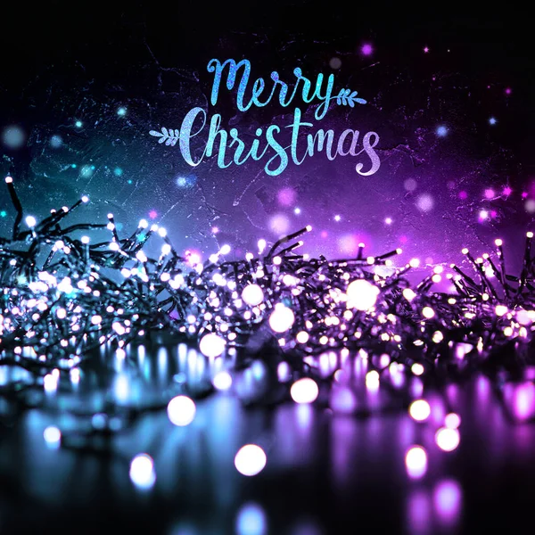 Sparkling Christmas lights in the evening at night on a dark background and the inscription Merry Christmas. Blue and purple color.