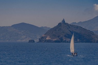 Bir yelkenlinin karaya çıktığı deniz manzarası. Küçük kayalık bir adanın üzerine inşa edilmiş eski bir deniz feneri konuyu gözden kaçırıyor. Gökyüzü açık ve havada hafif bir sis var. Bu da sıcak ve bunaltıcı bir hava olduğunu gösteriyor.