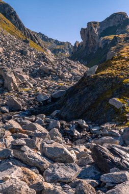 Yüzüklerin Efendisi tarzında Alp manzarası. Ön planda, arka plandaki yüksek dağlara doğru uzanan ve manzarayı gören çimenli bir alan var. Bir kız.