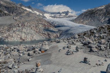 Alp kayalıkları manzarası, 2021 yazında Rhone Buzulu manzarası. Buzulun dibinde iklim değişikliğinin neden olduğu sürekli eriyen buzun oluşturduğu göl var. Gökyüzü...