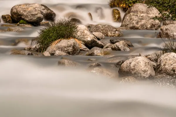 Long exposure and close-up detail of a river flowing between stones and clumps of grass. — Stock Photo, Image