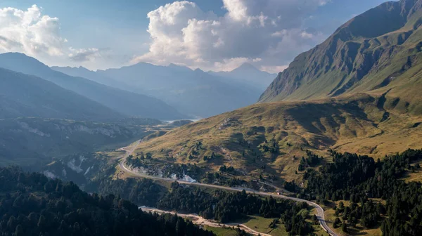 Aerial view towards the Lukmanier Pass, a mountain pass in the Swiss Alps in the canton of Graubunden. A rocky ridge on the right leads the eye towards the road that flows sinuously in the valley.