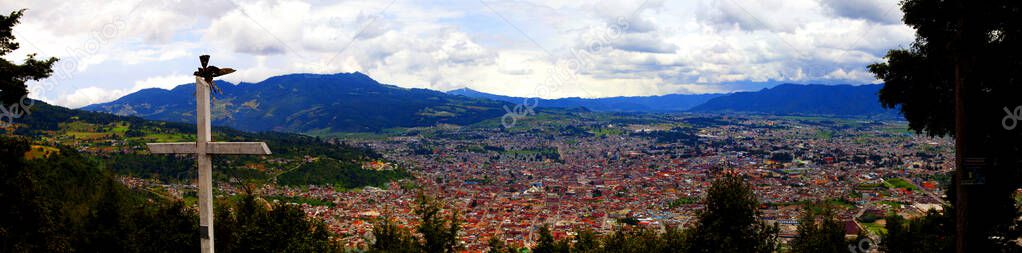 Panorama of mountains and town of Quetzaltenango with cross at top of lookout in Guatemala.