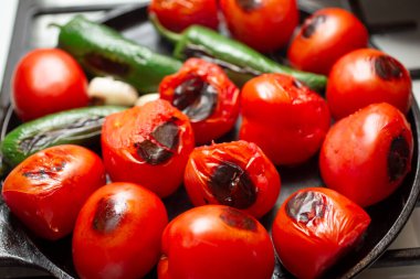 A closeup view of a salsa vegetable ingredients roasting on a comal.