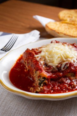 A closeup view of a lasagna plate with melted cheese, and a side of garlic bread, in a restaurant or kitchen setting.