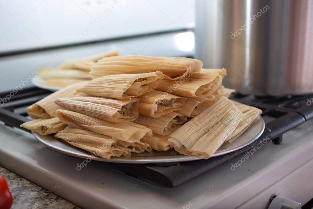 A view of a pile of tamales, ready for cooking, in a home kitchen setting.