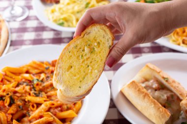 Arka planda birkaç İtalyan antresinin yer aldığı bir dilim sarımsaklı ekmeği tutan bir elin görüntüsü.