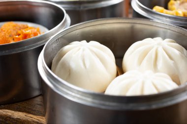 Çin baozi 'sinin çelik bir buharlı konteynırı, bir restoran veya mutfak ortamında, diğer çeşitteki hamur köftelerinin yanında..