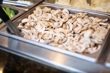 Yerel bir açık büfe restoranında görülen çiğ mantar dilimleriyle dolu bir buharlı tencere manzarası..